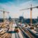 A bustling construction site with cranes, bulldozers, and workers building roads, bridges, and buildings for the planned UK infrastructure spending in 2025