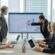 A group of professionals collaborating in a modern office, discussing charts and data on a large screen during a meeting, discussing QSRA and QCRA