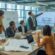 A group of professionals collaborating around a conference table with digital screens and blueprints, discussing infrastructure project plans.